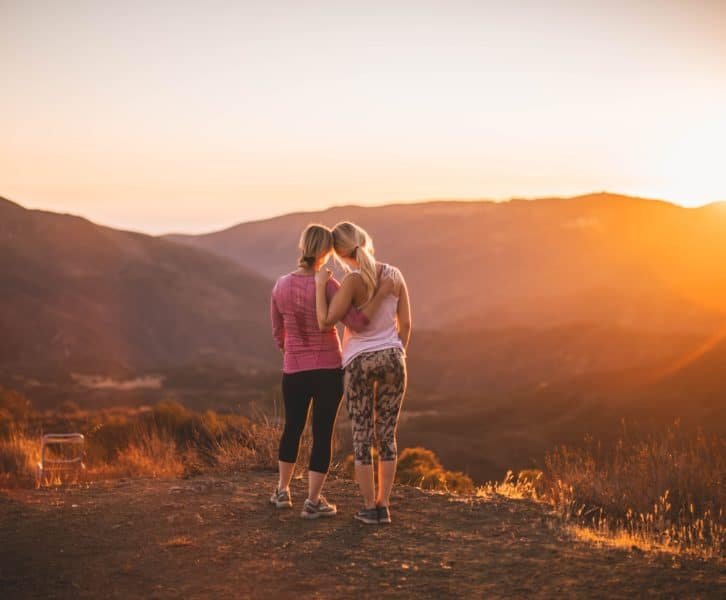 Two girls watching the sunset atop a mountain.
