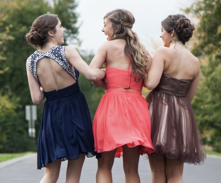 Three girls wearing varying formal dresses laughing, turned away from the camera